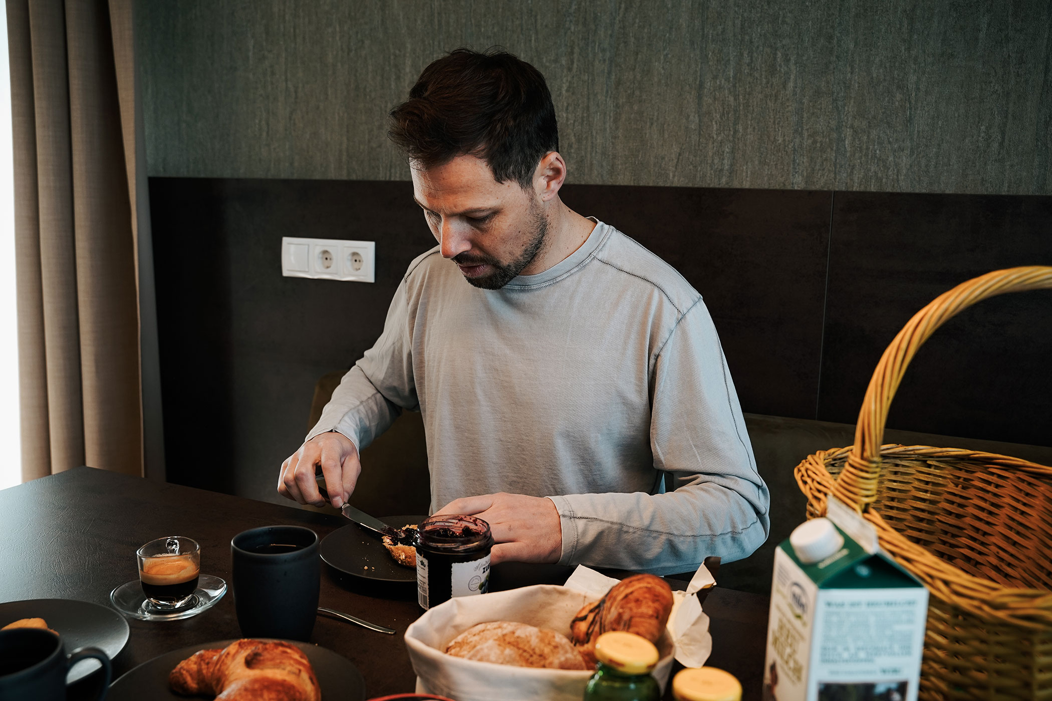 A man sits at the breakfast table and spreads a jam sandwich