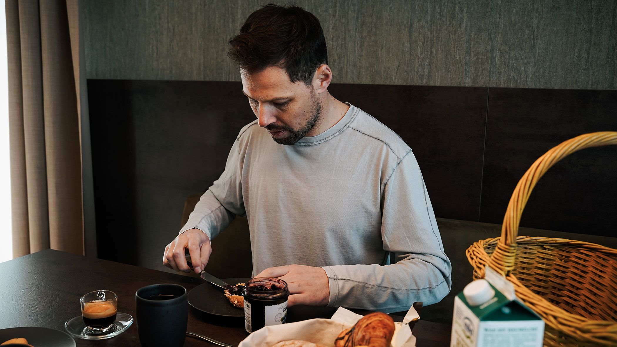 A man sits at the breakfast table and spreads a jam sandwich