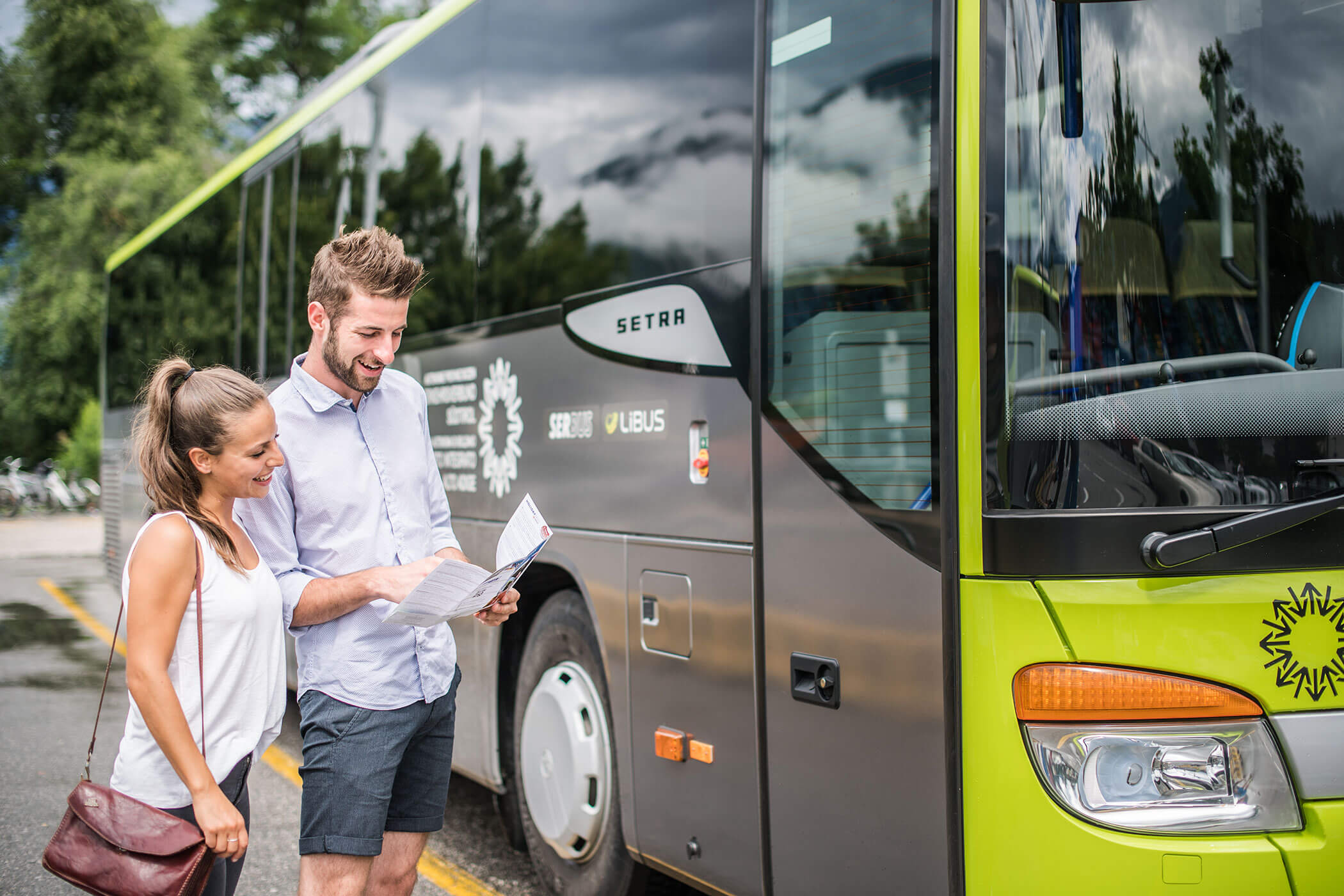 A couple stands in front of a bus and looks at a brochure